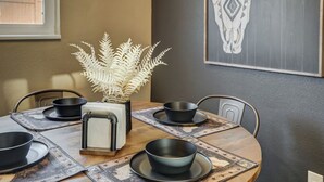 A dining table with black bowls and plates, a decorative vase with white foliage, and a wall-mounted artwork.