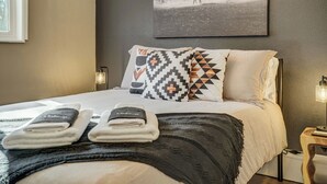 A hotel room with a bed, pillows, a blanket, and a wall-mounted picture.