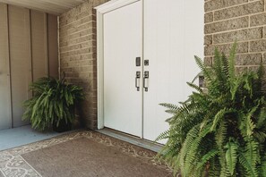 Una puerta con cerradura electrónica, una planta en maceta y un felpudo estampado.