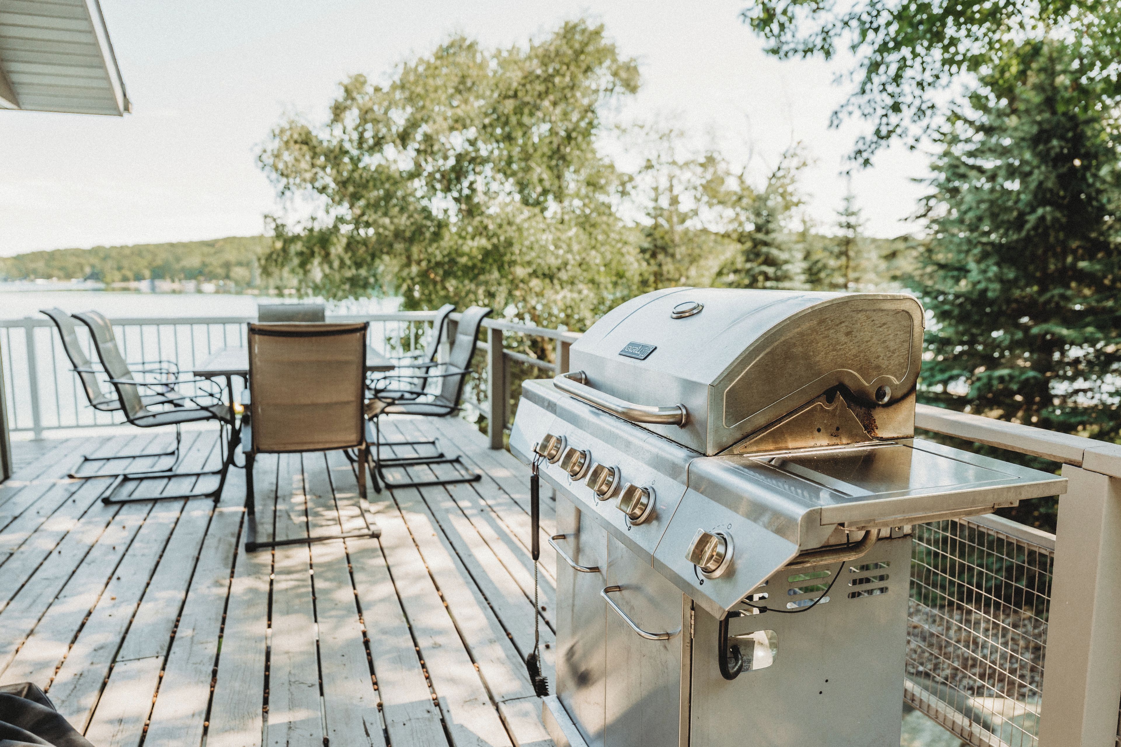 An outdoor deck with a grill, chairs, and a table.