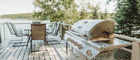 An outdoor deck with a grill, chairs, and a table.