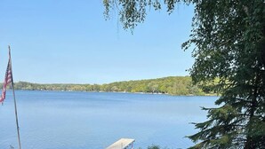 Une terrasse avec des fauteuils Adirondack et un foyer extérieur, le tout offrant une vue sur un lac.