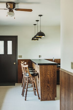 A kitchen with a central island, wooden bar stools, pendant lights, and a ceiling fan.