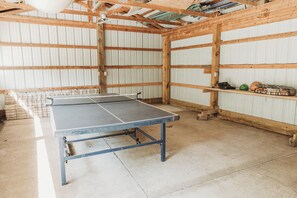 Una mesa de ping pong en una habitación con vigas de madera y paredes de metal corrugado.