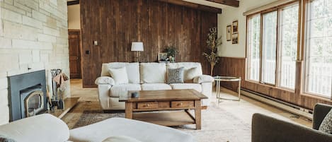 A living room with a fireplace, a sofa, a coffee table, and a large window.
