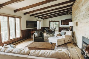 A spacious living room with a high ceiling, wooden beams, a fireplace, and a dining area with a table and chairs. - Lilac Retreat lake house sauna + pickleball close to St. Johns and St. Bens (Saint Joseph)