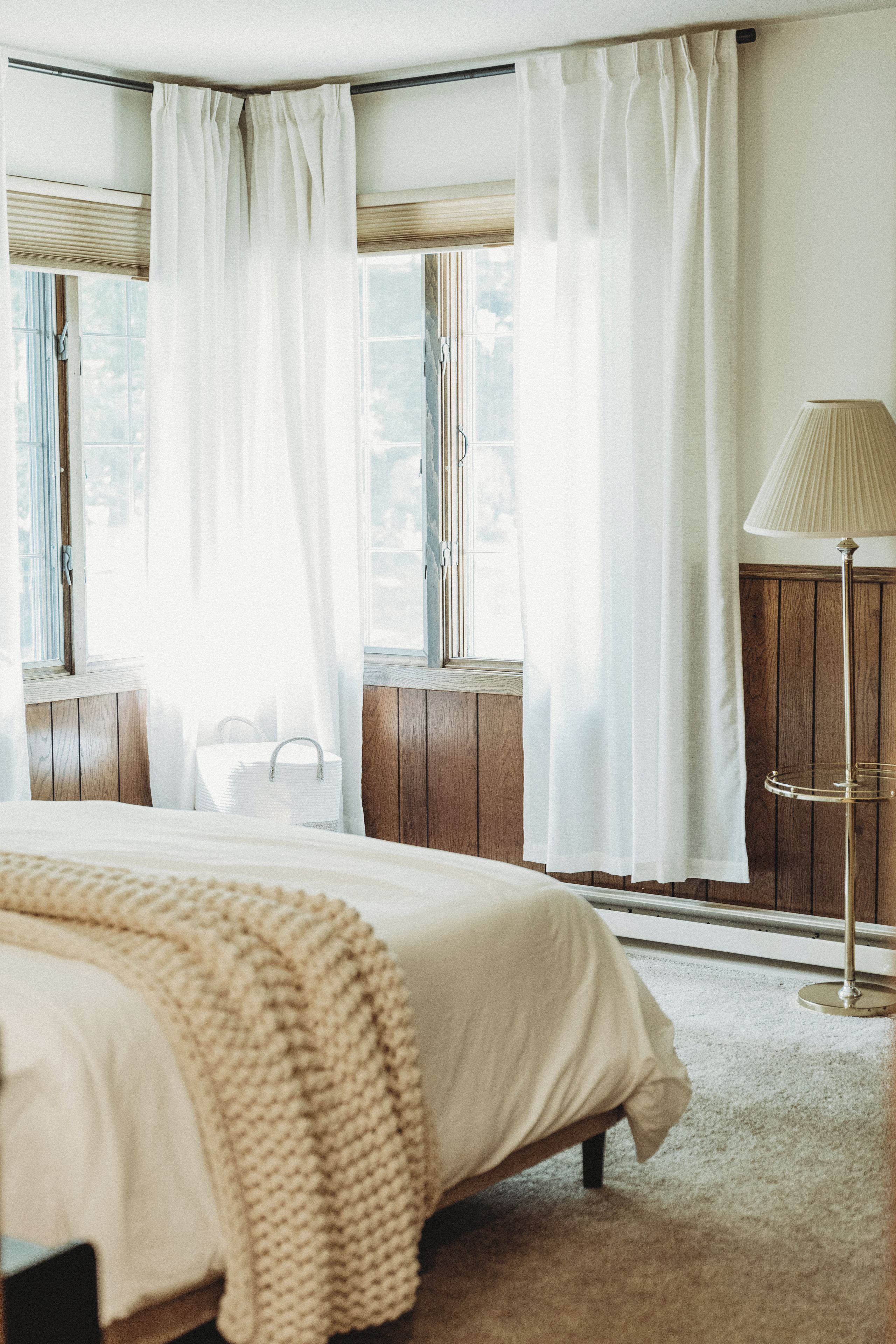A bedroom with a bed, a bedside table, a lamp, and a window with curtains.