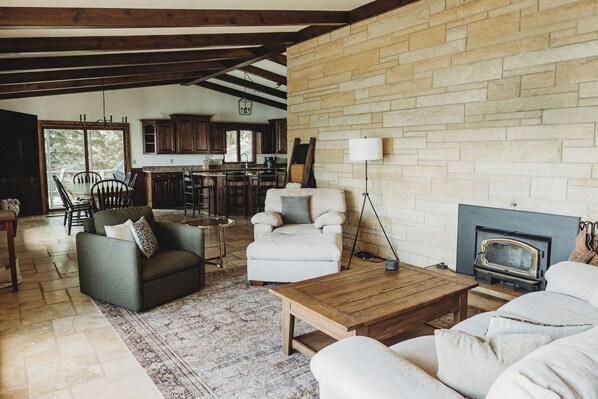 Un salón amplio con chimenea, un comedor con cocina al fondo, y un ventanal grande que proporciona luz natural.