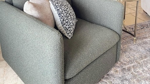 Un salon avec un canapé gris, une table basse en verre et un coussin à motifs.