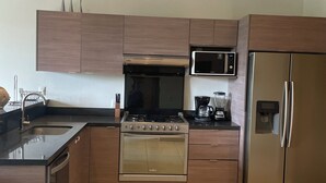 Une cuisine moderne avec des meubles en bois, un réfrigérateur en acier inoxydable, un four à micro-ondes, une cuisinière et une machine à café.
