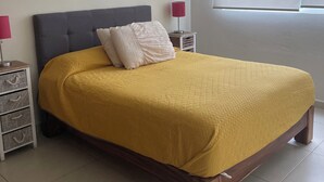 Une chambre à coucher avec un lit, une table de chevet, une lampe et une fenêtre donnant sur des palmiers.