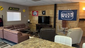 Una sala de estar con un sofá de cuero marrón, una silla blanca, una mesa de centro de granito, un televisor y paneles de madera en las paredes.