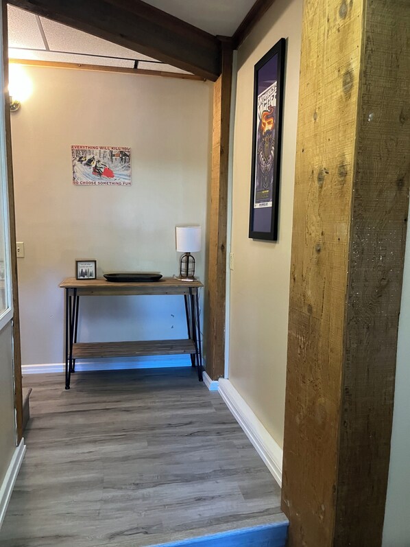 A hallway with a wooden floor, a desk with a lamp, and a poster on the wall.