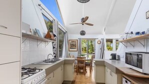 A compact kitchen with white cabinets, a gas stove, a microwave, and a ceiling fan. - Hook Wine and Sinker (Gympie)