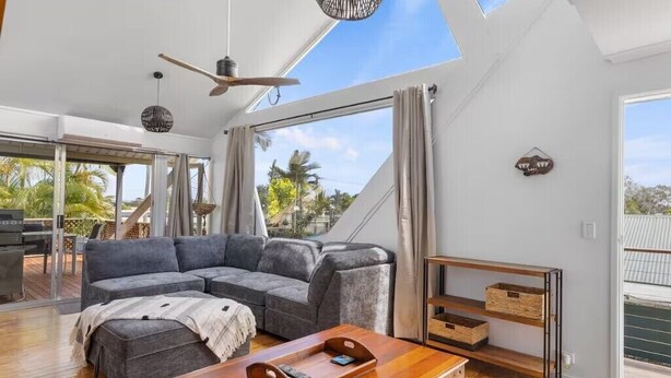 A spacious living area with a large gray sectional sofa, a wooden coffee table, and a ceiling fan. - Hook Wine and Sinker (Gympie)