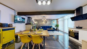 A modern kitchen with a dining area, featuring a central island, yellow chairs, a blue sofa, and a TV mounted on the wall. - House with Spa and Private Sauna (Lissac-sur-Couze)