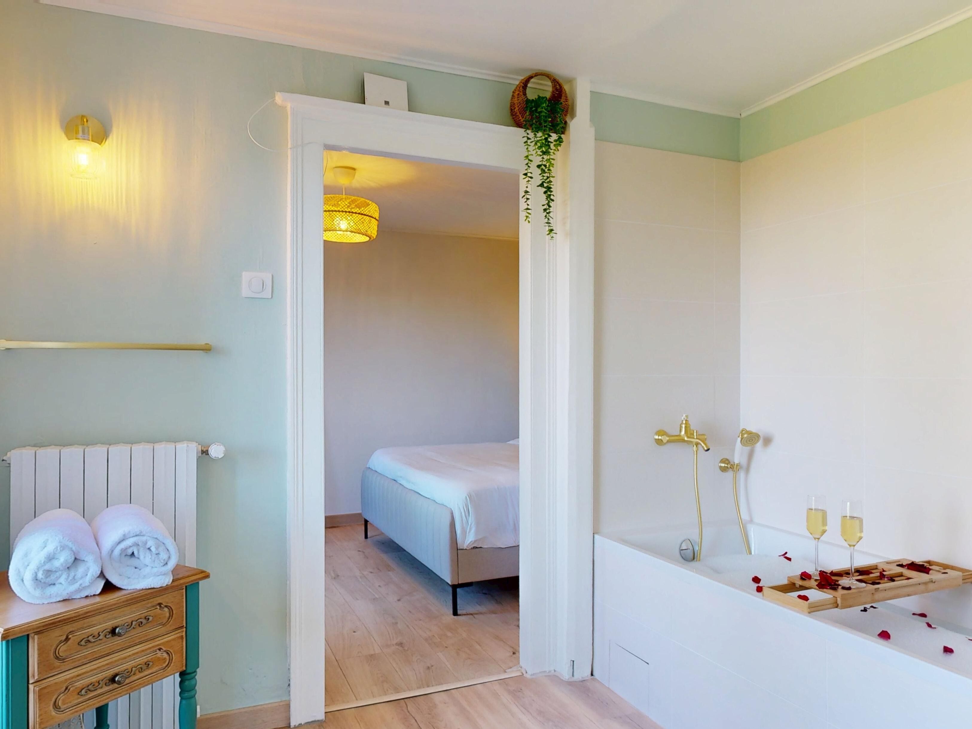 Ein Hotelzimmer mit Bett, einem Holzschrank mit Handtüchern, einem Badezimmer mit Badewanne und einer hängenden Pflanze.