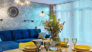 A modern living room with a blue sofa, a dining table with yellow plates and glasses, and a wall clock. - House with Spa and Private Sauna (Lissac-sur-Couze)
