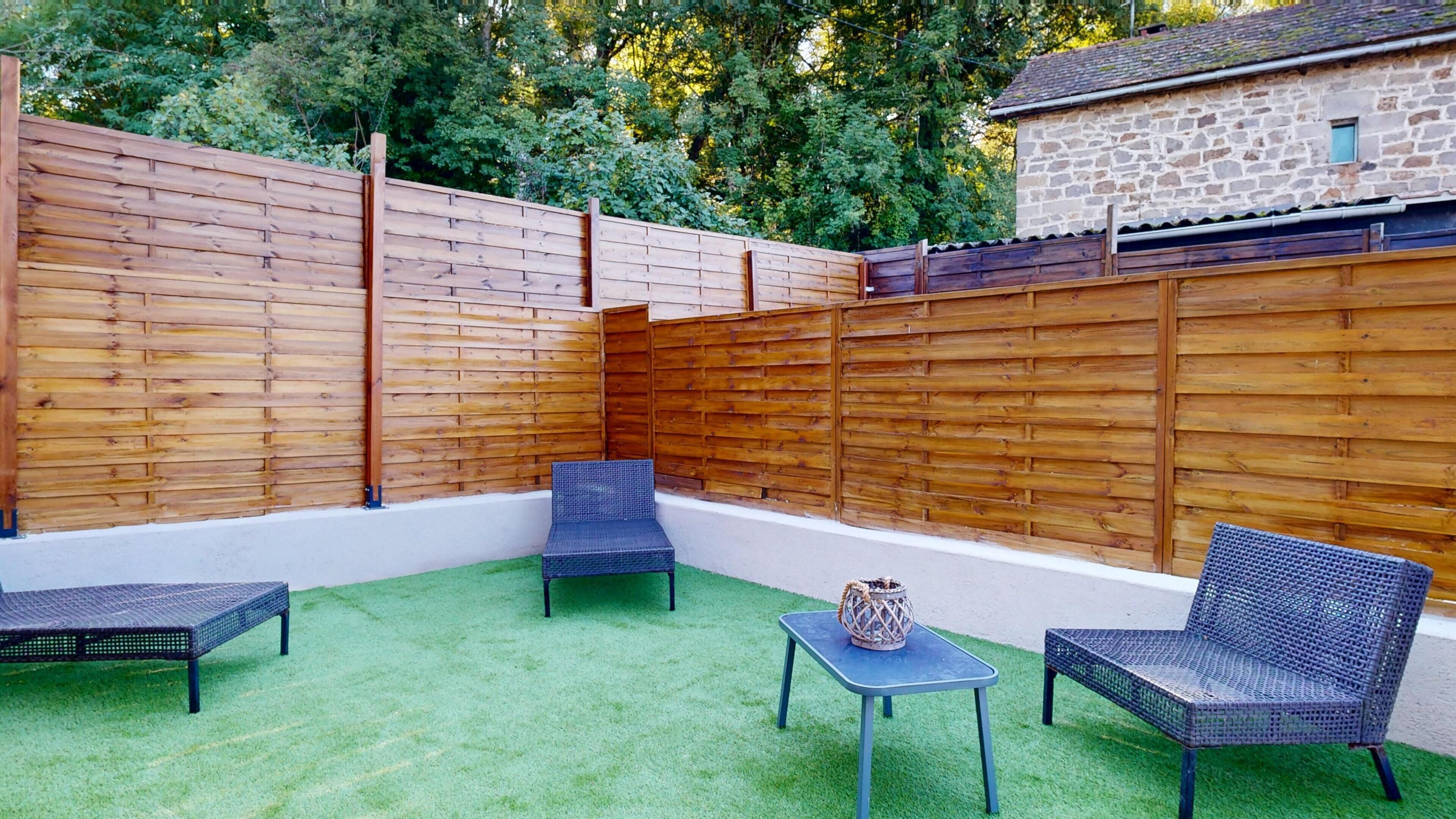 A patio with a wooden fence, two wicker chairs, a small table, and a decorative basket.