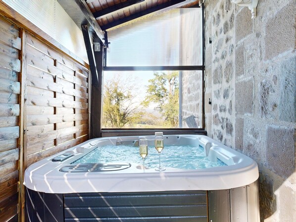 A hot tub with two glasses of champagne, a wooden wall, and a stone wall with a window.
