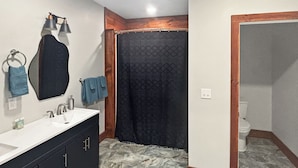 Une salle de bain avec un lavabo blanc, des meubles noirs, un miroir et un rideau de douche.