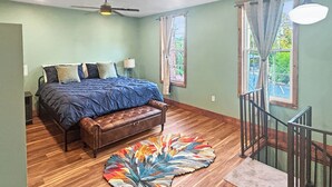Une chambre à coucher avec un lit, un banc, un tapis coloré, un ventilateur de plafond et un escalier.