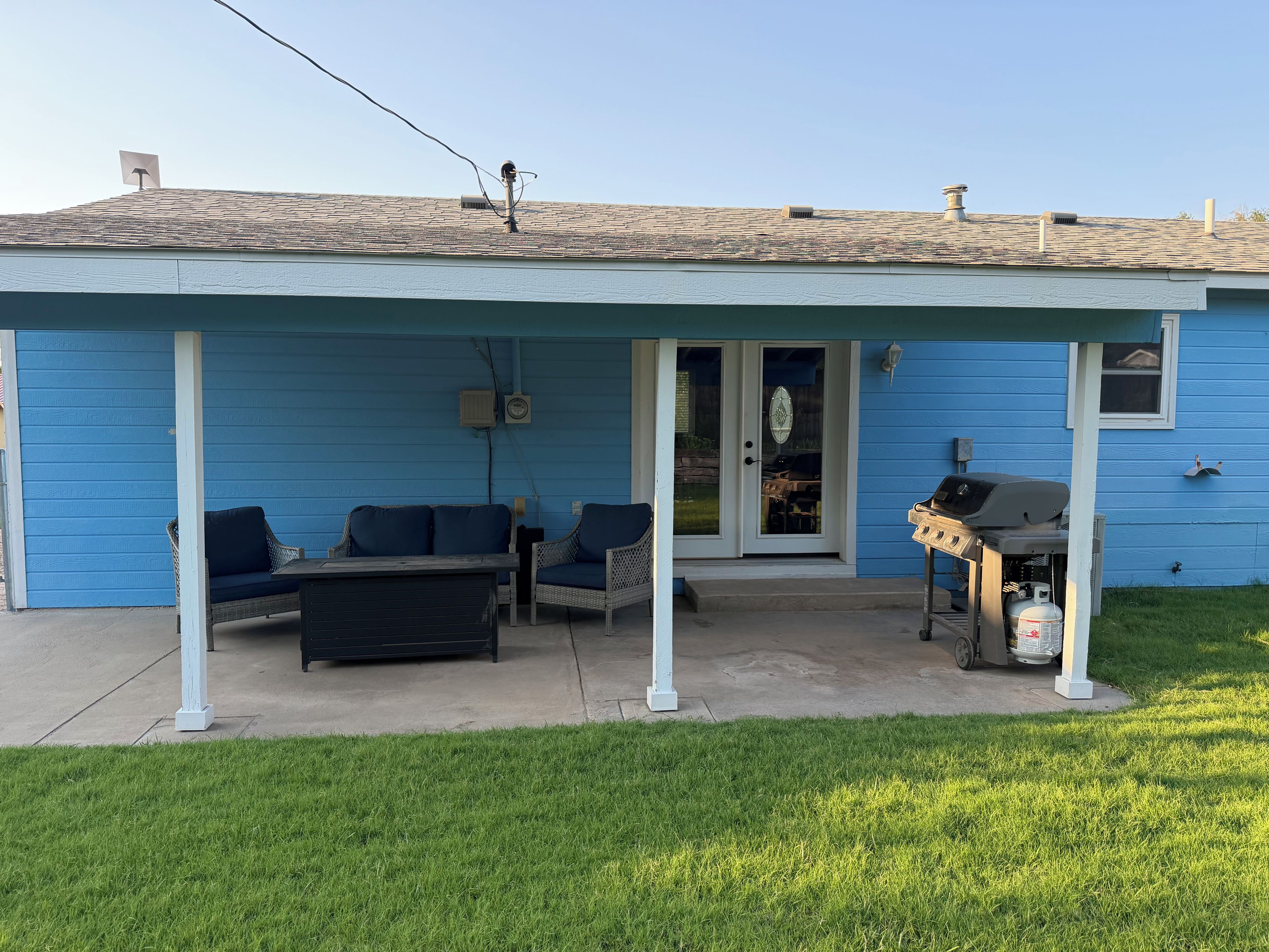 Uma casa azul com varanda coberta, móveis de jardim e churrasqueira.