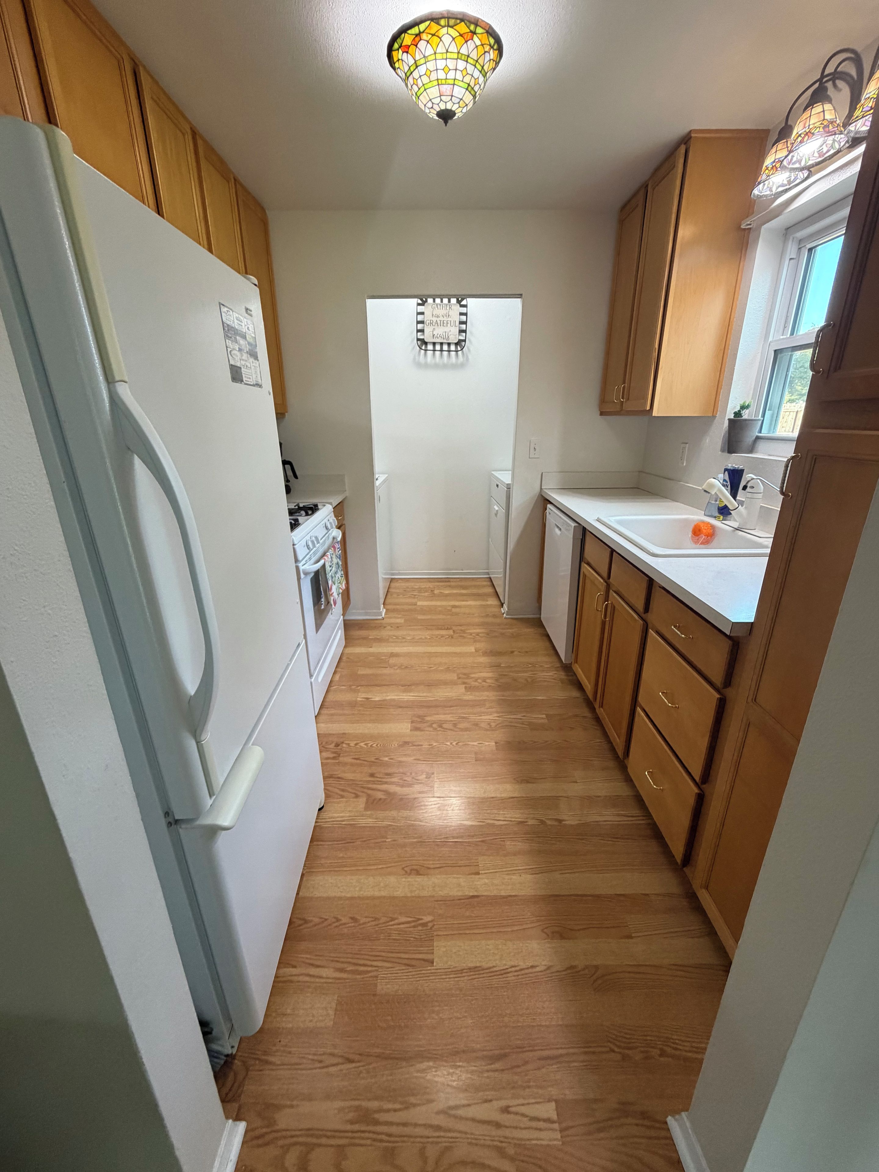 Une cuisine étroite avec des meubles de rangement en bois, un réfrigérateur blanc et un plancher en bois.