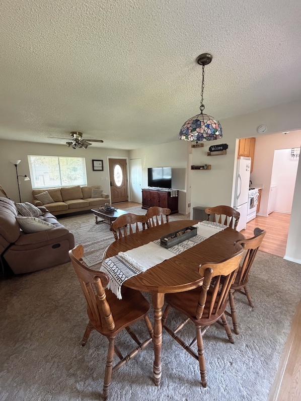 A living room with a sofa, a dining table with chairs, a TV, and a ceiling fan. - Little Blue: A Cozy 3-bedroom, 1-bath home. (Lamar)