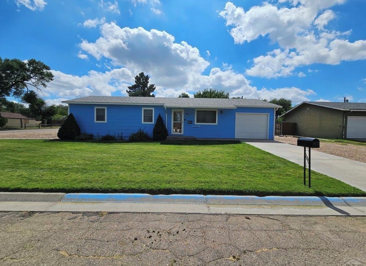 Une maison d’habitation à un étage, à l’extérieur bleu, avec une pelouse bien entretenue dans le jardin avant et une porte de garage.