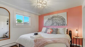 Ein Schlafzimmer mit einem Bett, einem großen Spiegel, einem Fenster, einem Wandbild und einem Nachttisch mit Lampe.