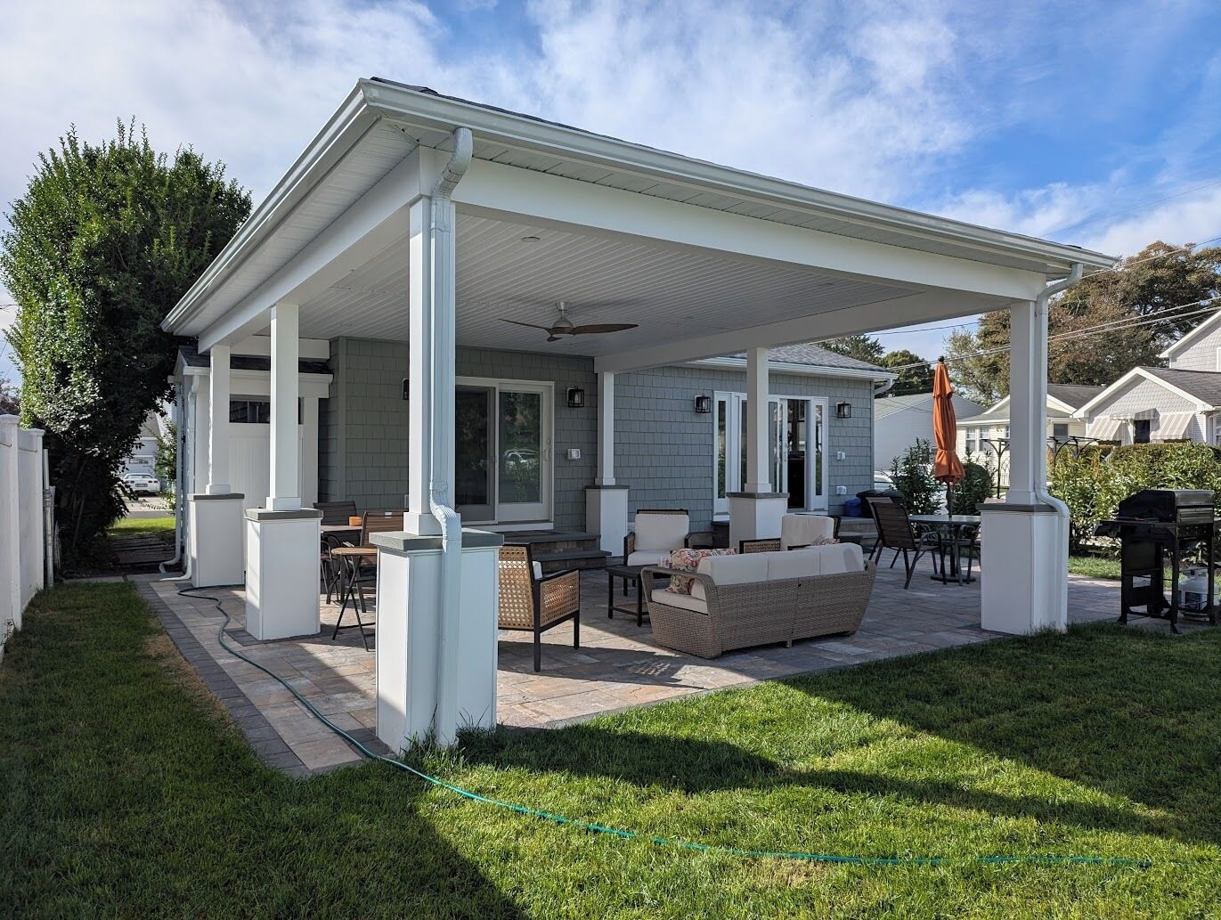 Un patio couvert, aménagé avec du mobilier d’extérieur et doté d’un ventilateur de plafond, offrant une vue sur le jardin arrière.