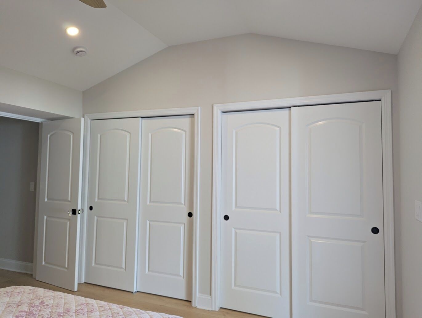 A room with a large closet containing four white doors, a ceiling fan, and a light fixture.