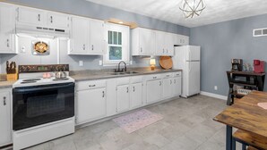 A modern kitchen with white cabinets, a built-in oven, a sink, and a wooden dining table. - The Yellow Haus, close to downtown Waterloo! (Waterloo)