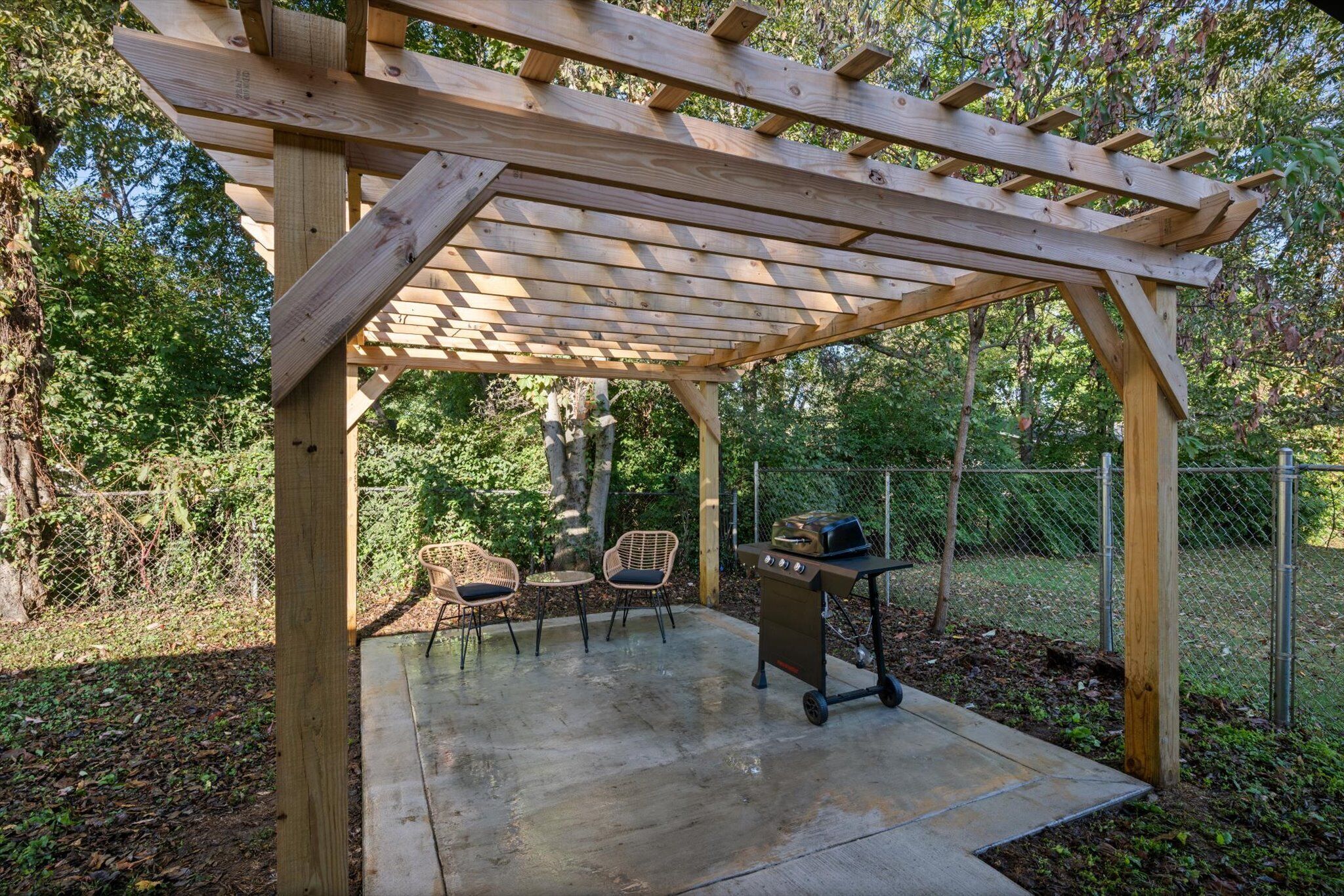 A wooden pergola structure with a grill and seating area.