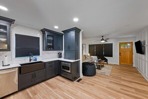 A modern kitchen with dark cabinets, a white countertop, and a built-in oven. There is a dining area with a black bean bag chair and a wooden table. - Newly Renovated Family Retreat (Franklin)