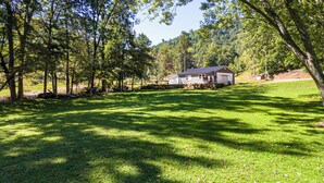 Une maison avec des fondations en pierre, entourée d’une cour verdoyante et d’arbres.