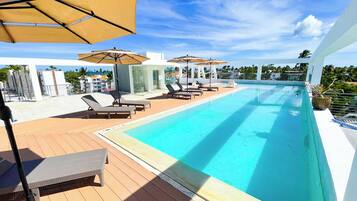 Una piscina al aire libre, sombrillas, sillones reclinables de piscina