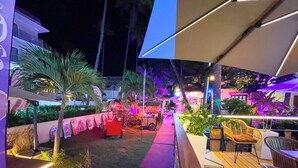 An outdoor patio area with a wooden deck, seating arrangements, and a pathway leading to a building. - STUDIOS ROOFTOP POOL & BEACH (Punta Cana)