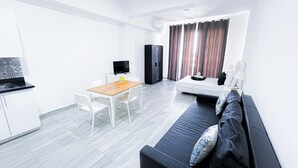 Een moderne woonkamer met een bank, een eettafel met stoelen, een televisie en een keuken met kasten en een aanrecht.