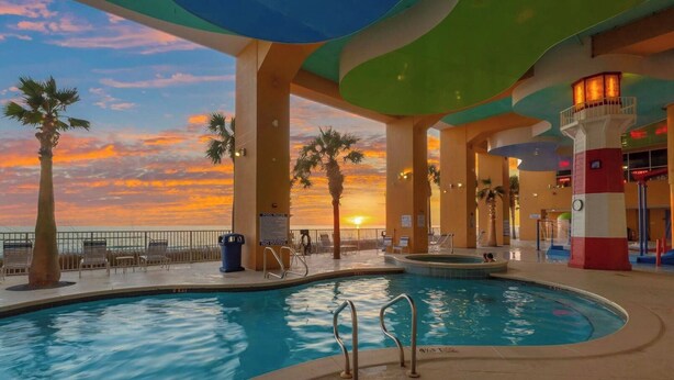 An indoor swimming pool with a sunset view, lounge chairs, and palm trees. - Spacious 3BR/3BA Splash Condo & Amazing Gulf Views — Free Beach Chairs Included! (Panama City Beach)