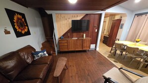 A cozy living room with a brown leather sofa, a wooden bench, and a dining area with a table and chairs. - Delightful cottage in charming Mount Gretna in an amazing location! (Mount Gretna)