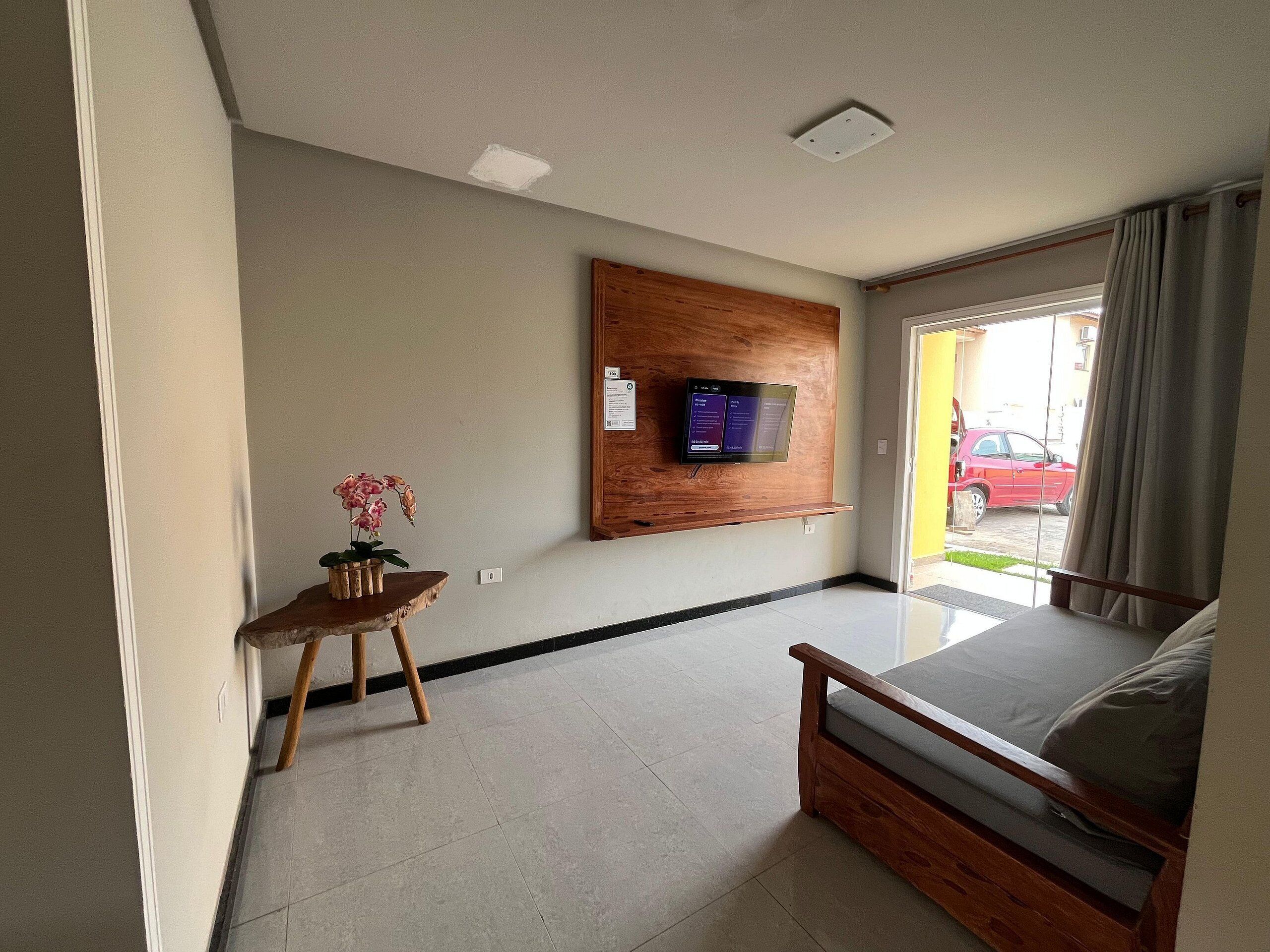 Habitación de hotel con cama, una pequeña mesa de madera con una orquídea, televisor montado y vista a un coche rojo en el exterior.