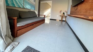 A modern living room with a sofa, a flat-screen TV mounted on the wall, a small wooden side table, and a large painting of a beach scene. - Condomínio Tranquilo 350m da Praia (Porto Seguro)