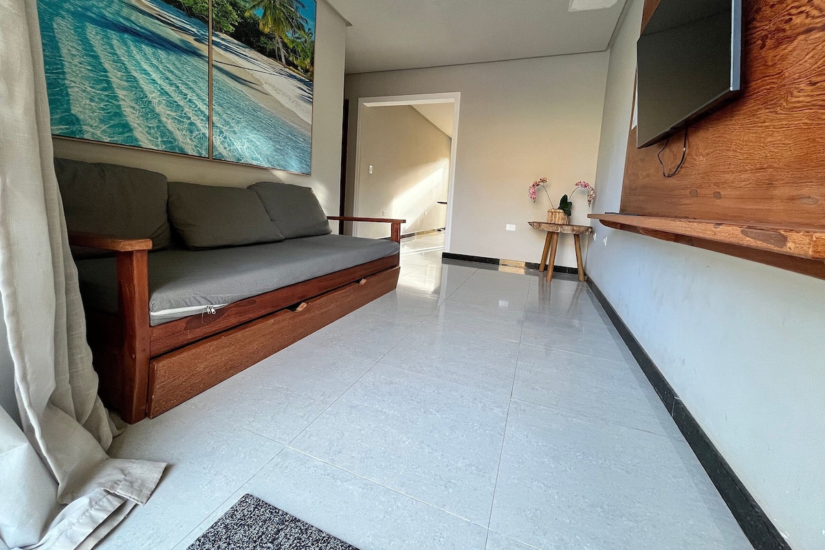 Un salon moderne avec un canapé, un téléviseur à écran plat fixé au mur, une petite table d’appoint en bois et un grand tableau représentant une scène de plage.