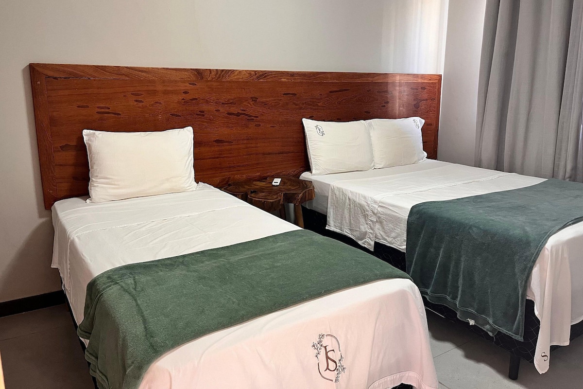 Une chambre d’hôtel avec deux lits, une tête de lit en bois, du linge de lit blanc et une couverture verte.