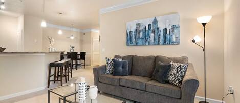 A living room with a gray sofa, a glass coffee table, and a cityscape painting on the wall.