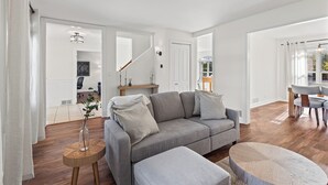 A spacious living room with a grey sofa, a round wooden side table, and a matching ottoman.