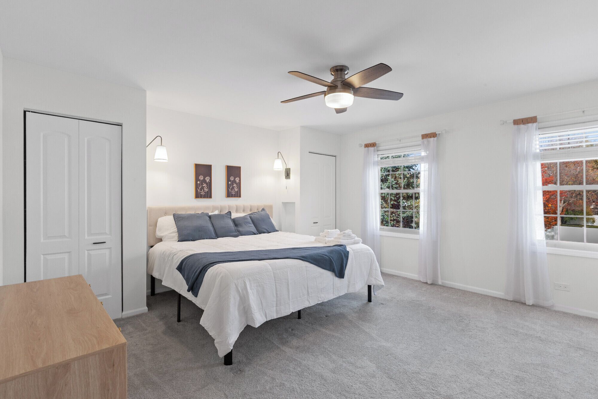 Une chambre à coucher avec un lit, un ventilateur de plafond, une fenêtre avec des rideaux et une porte.