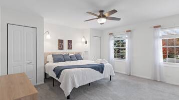 Une chambre à coucher avec un lit, un ventilateur de plafond, une fenêtre avec des rideaux et une porte.